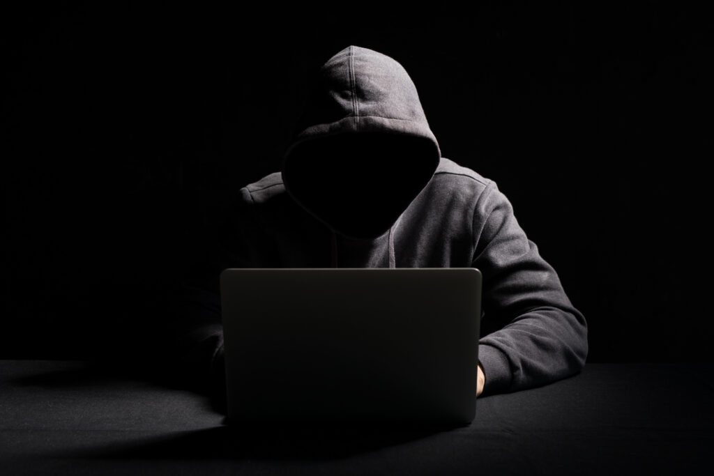 A hacker in a hoodie using a laptop in a dark room