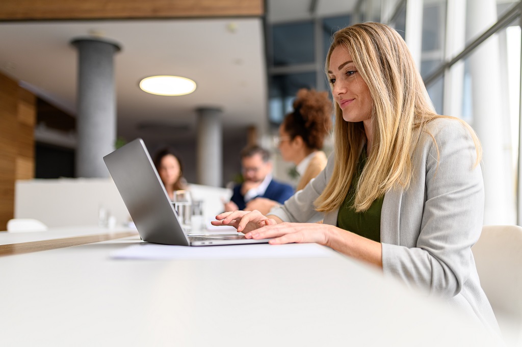A businesswoman using a laptop in an office, with co-workers in the background