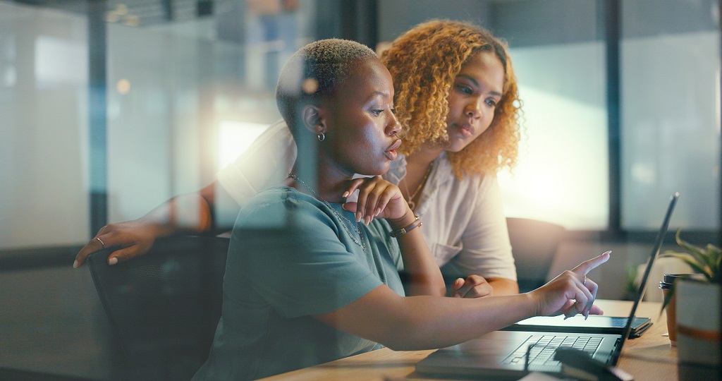 Two businesswomen in an office discussing something over a laptop