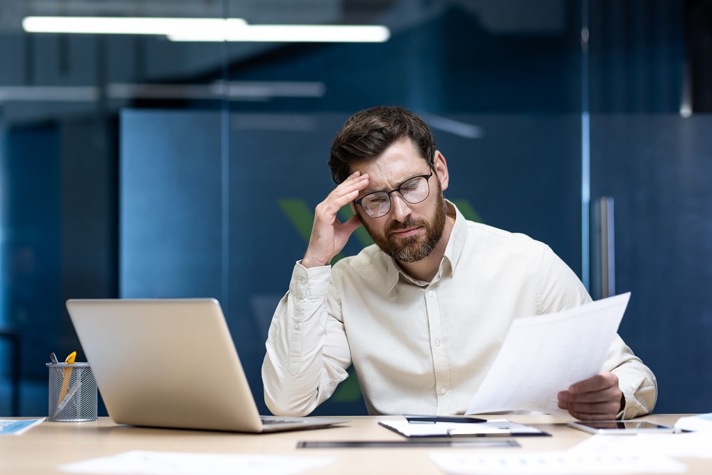 A worried male executive in an office using his laptop and analyzing a document