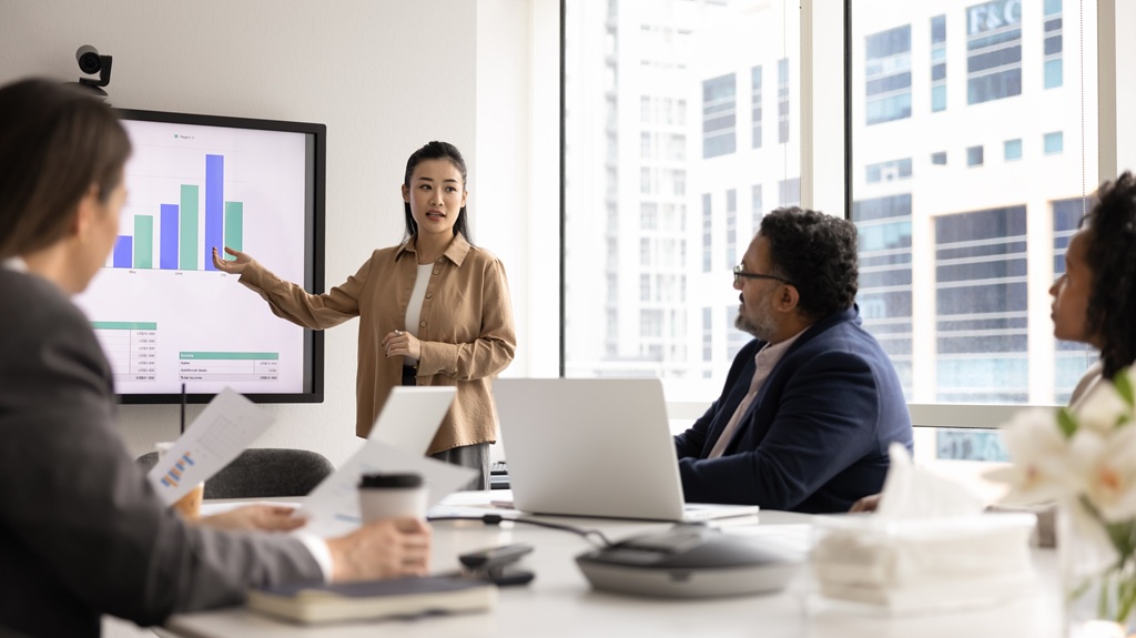 A female security specialist presents a cybersecurity report on a large screen to the board, explaining the metrics.